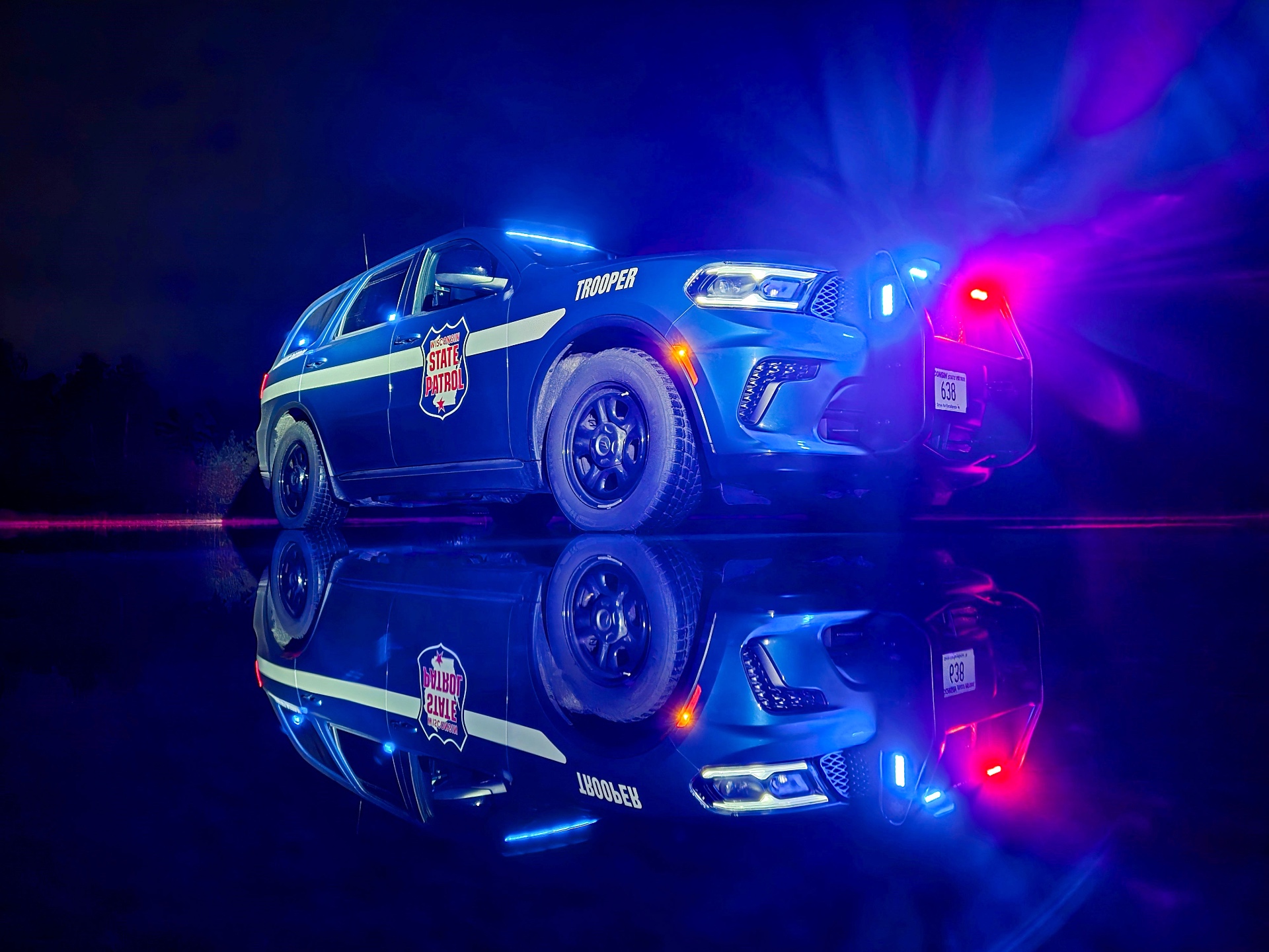 Wisconsin State Patrol trooper cruiser with emergency lights reflected on wet pavement at night